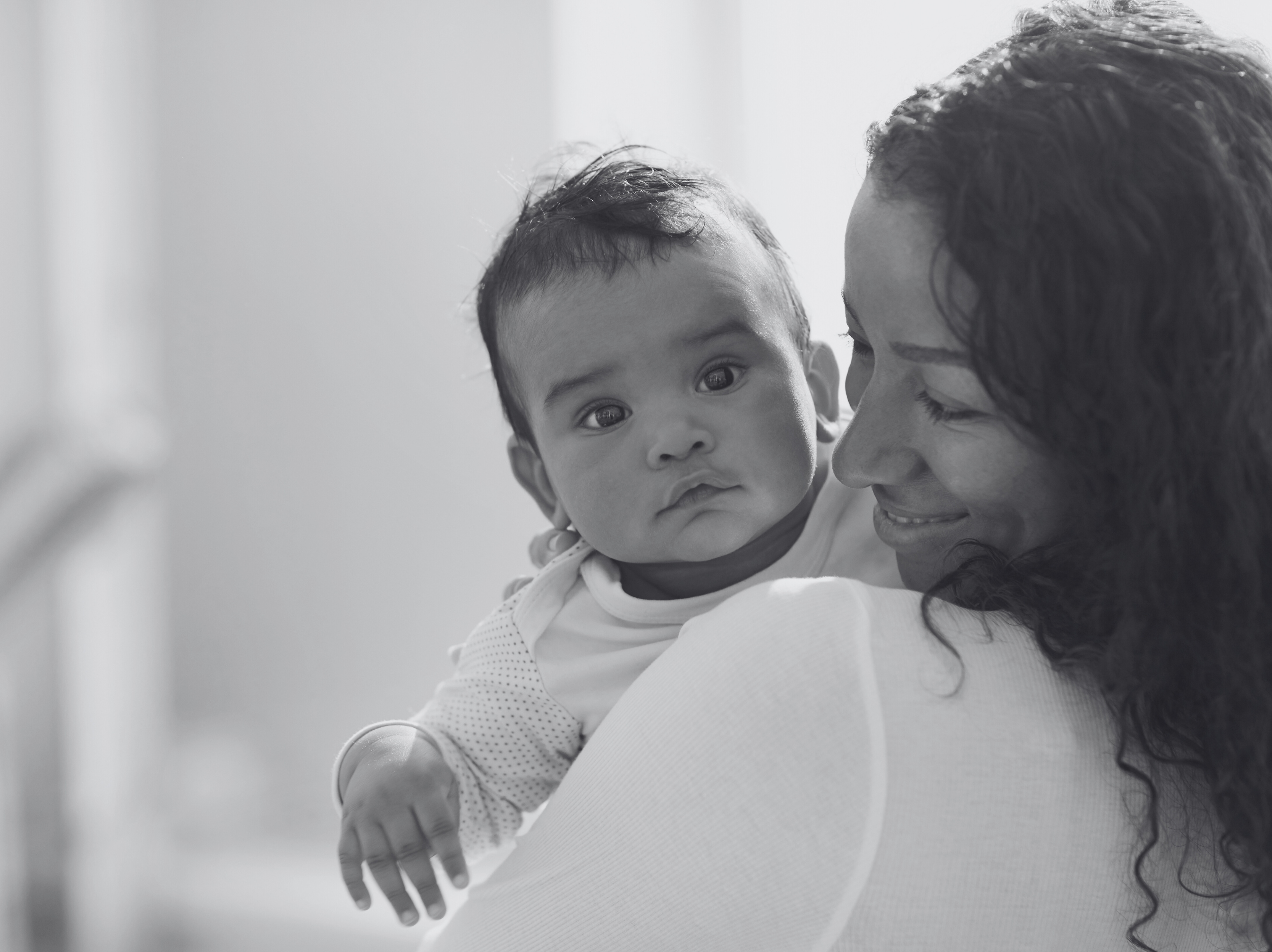 a mother holds her baby and smiles as the baby looks at the camera